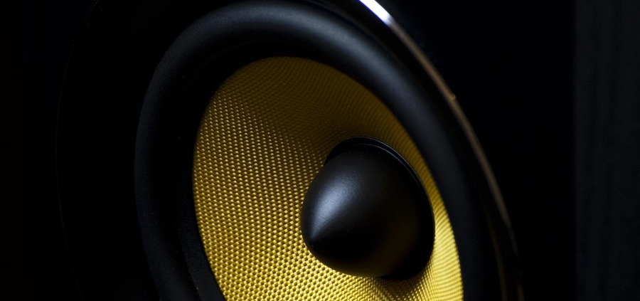 Close-up view of gold meshed speaker bass driver enclosed in a black cabinet.