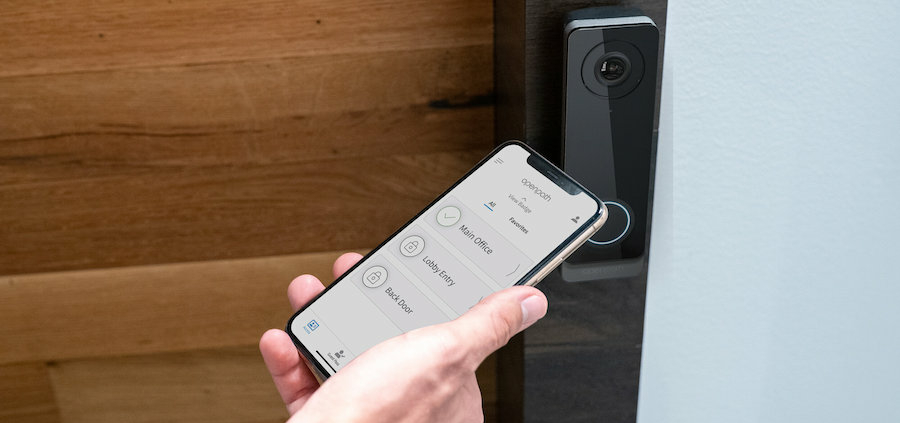 A smartphone is being held by an access control reader to open a door.
