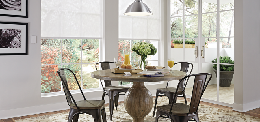 A dining space with two windows featuring motorized shades lowered halfway.