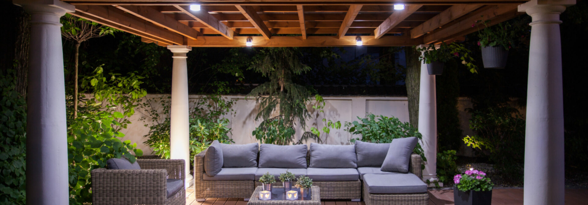 A pergola with a couch, a table, and motorized outdoor shades.