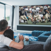 A couple snuggles in their private home theater while watching a football game.