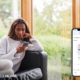 A woman relaxes on a couch, looking at her phone. A side image shows the Crestron Home app with Spotify playing audio in the living room.