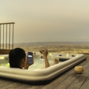 A woman in an outdoor spa checks her home settings on her phone.